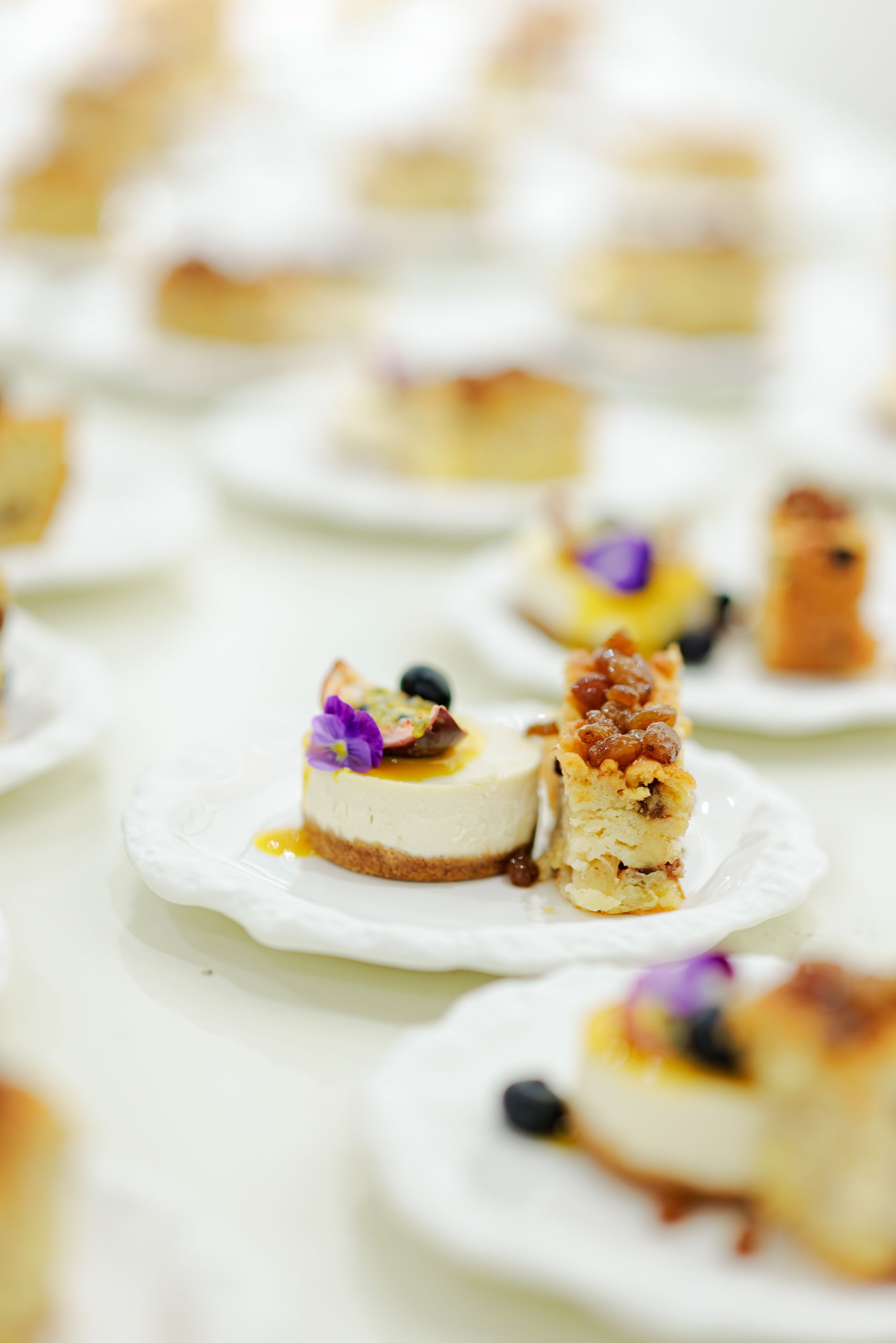 Elegant catering appetizers with purple edible flowers served on white plates in soft focus.