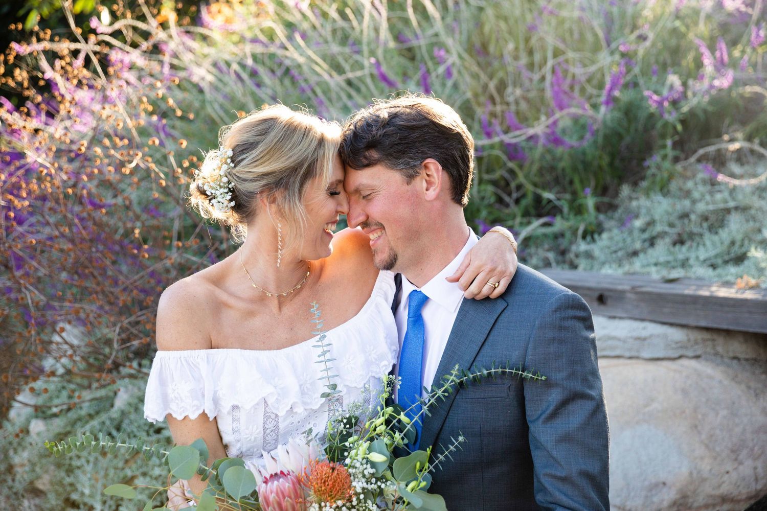 Romantic wedding couple poses among lavender flowers in garden setting.