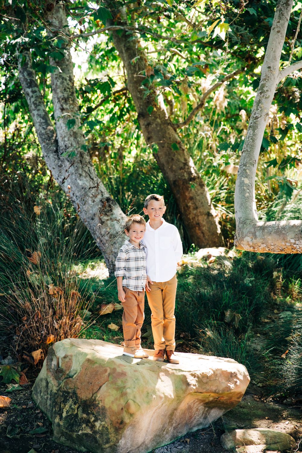 Two people explore a rocky area surrounded by lush green trees.