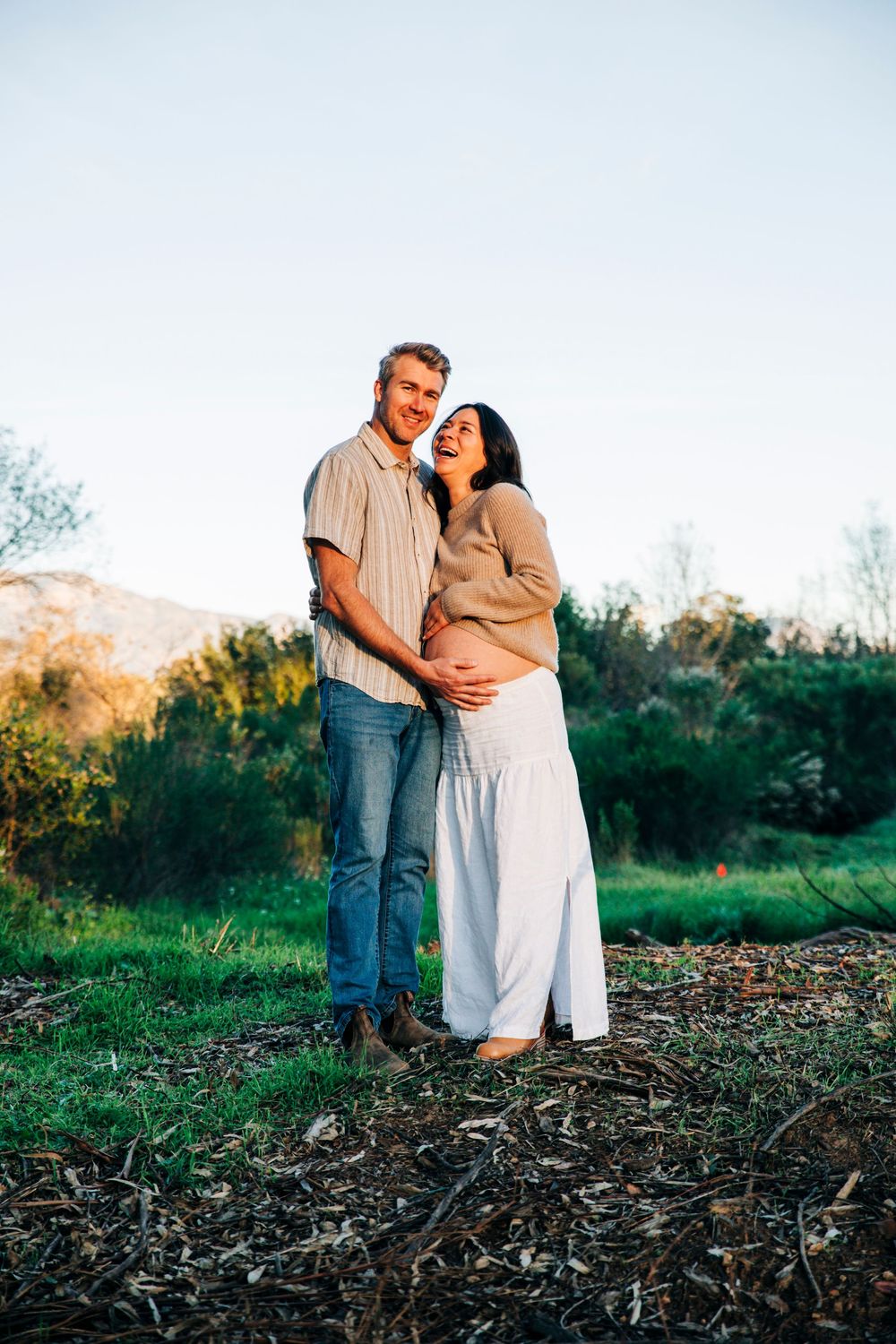 A couple embraces in a field during golden hour while wearing casual attire.