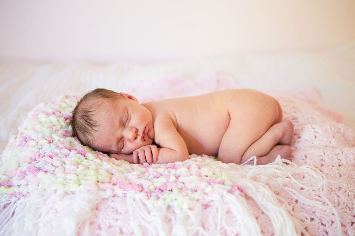 Sleeping newborn baby on pink floral blanket in soft natural lighting.