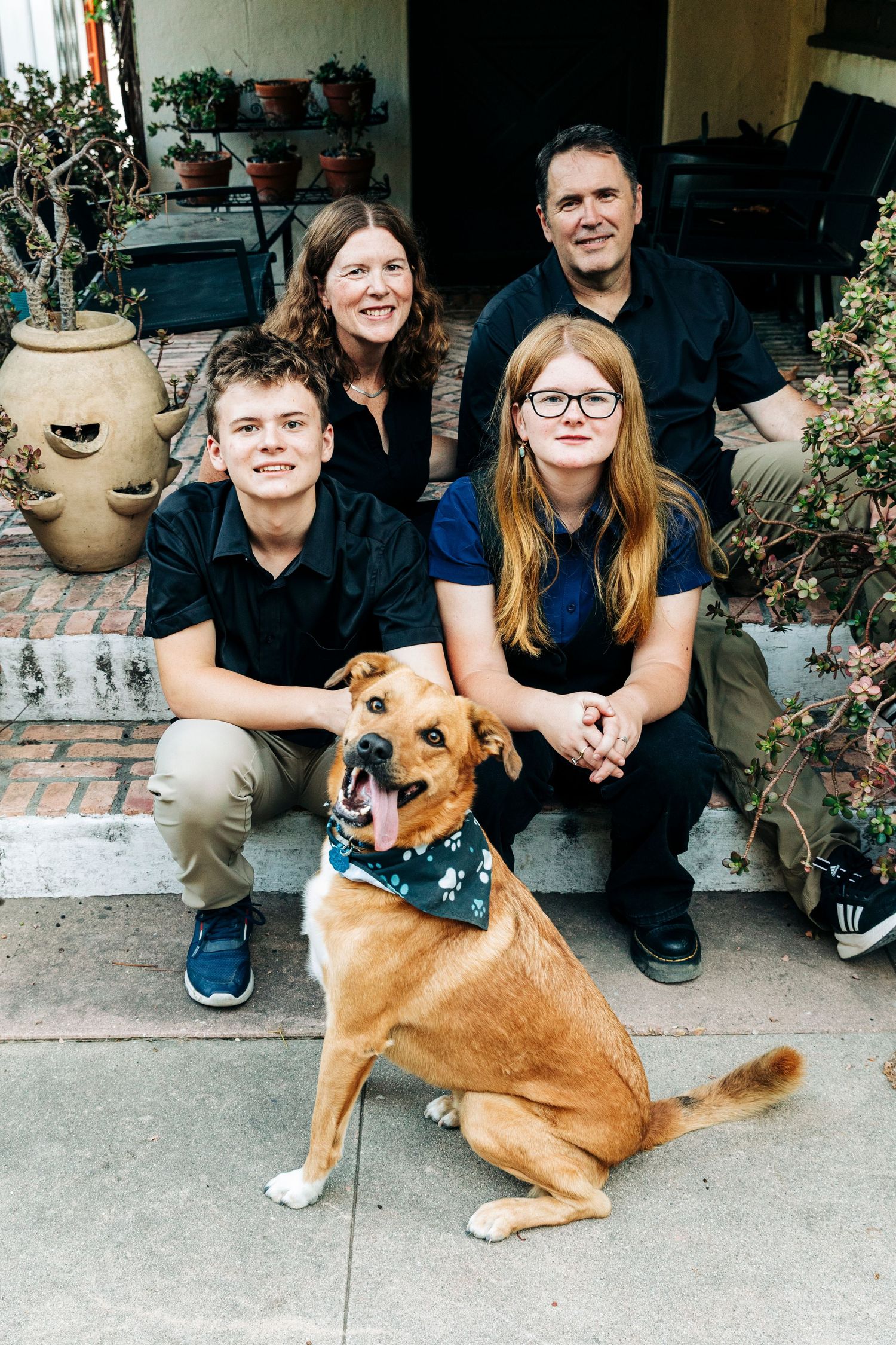 Family sitting together on porch steps with their brown dog wearing a bandana.