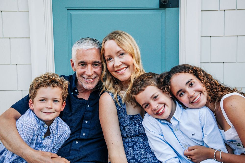 A relaxed family portrait on a porch featuring coordinated blue outfits and their pets.