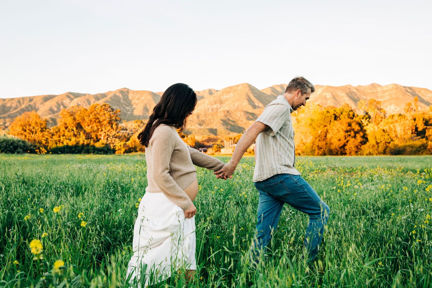 Romantic couple playfully running through a sunlit meadow during golden hour.