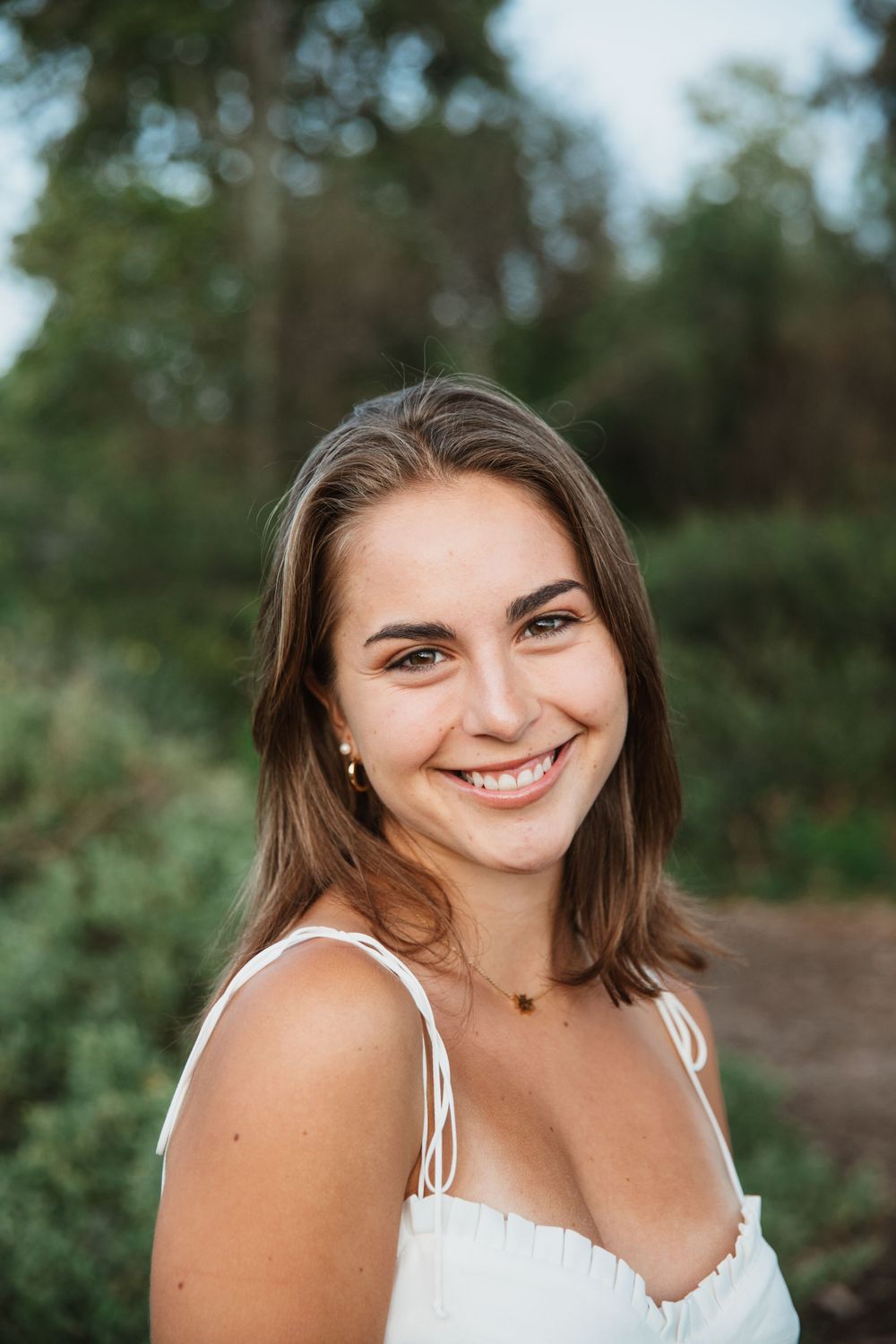 Woman in white summer dress smiling brightly in natural outdoor setting.