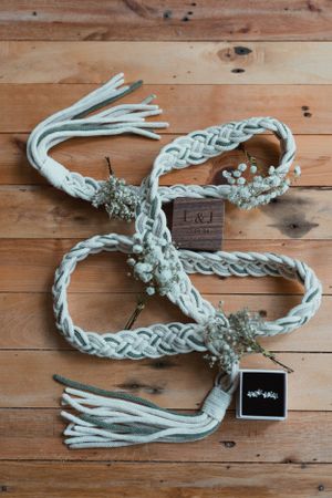 A braided white handfasting cord with baby's breath accents and tassels on wooden background.