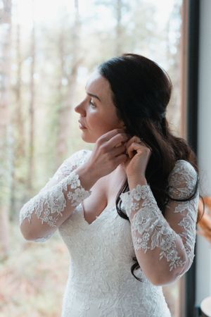 Artistic black and white photo showing wedding dress details near window.