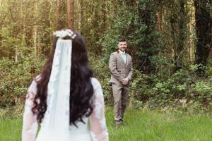 A couple poses together outdoors surrounded by lush green trees and foliage.