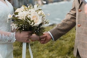 White floral wedding bouquet being passed between hands outdoors.