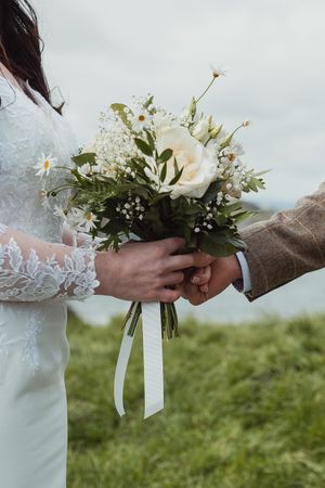 Close-up of hands holding a delicate white floral wedding bouquet with ribbons.