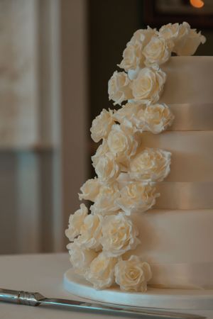 An elegant white wedding cake decorated with cascading white roses against a blurred background.