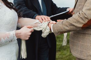 Close-up of hands exchanging wedding rings during an outdoor ceremony.
