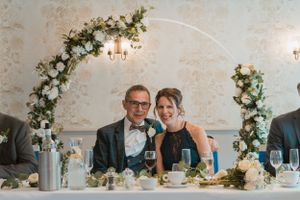 A wedding reception table setting with a floral arch and elegant table decorations.