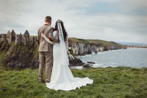 A wedding couple stands together on dramatic coastal cliffs overlooking the ocean.