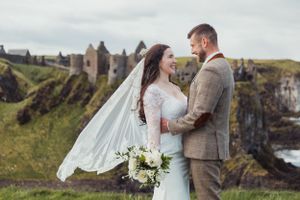 A romantic wedding portrait captured on scenic coastal cliffs with castle ruins in background.