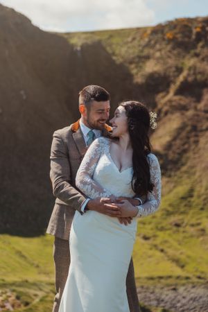 A romantic wedding photoshoot on a scenic hillside with the couple embracing in matching formal attire.