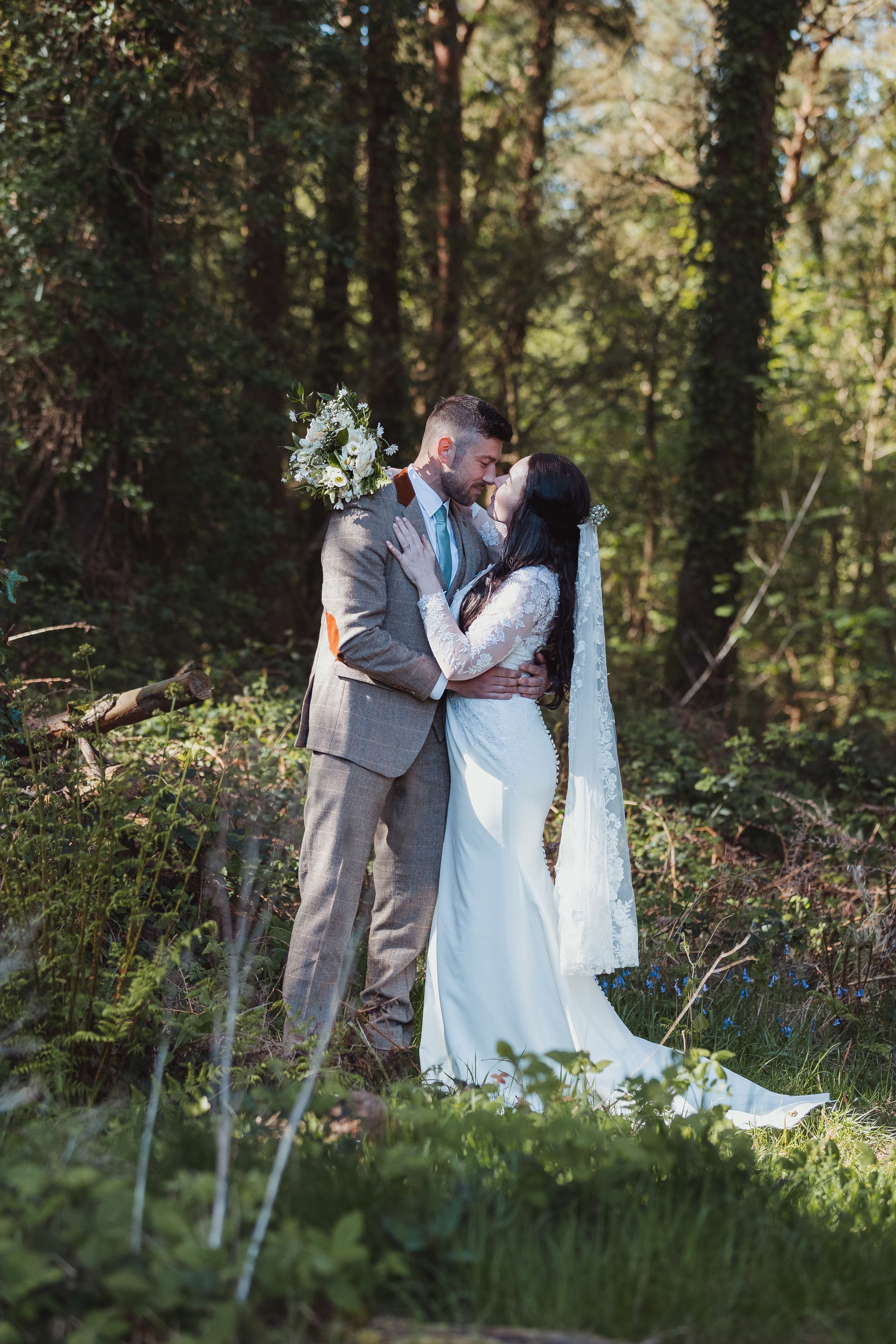 Wedding photography session in a lush wooded area with natural sunlight filtering through trees.