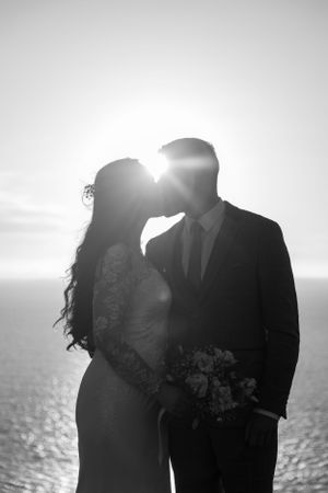 A silhouetted wedding portrait against a sparkling ocean horizon at sunset.