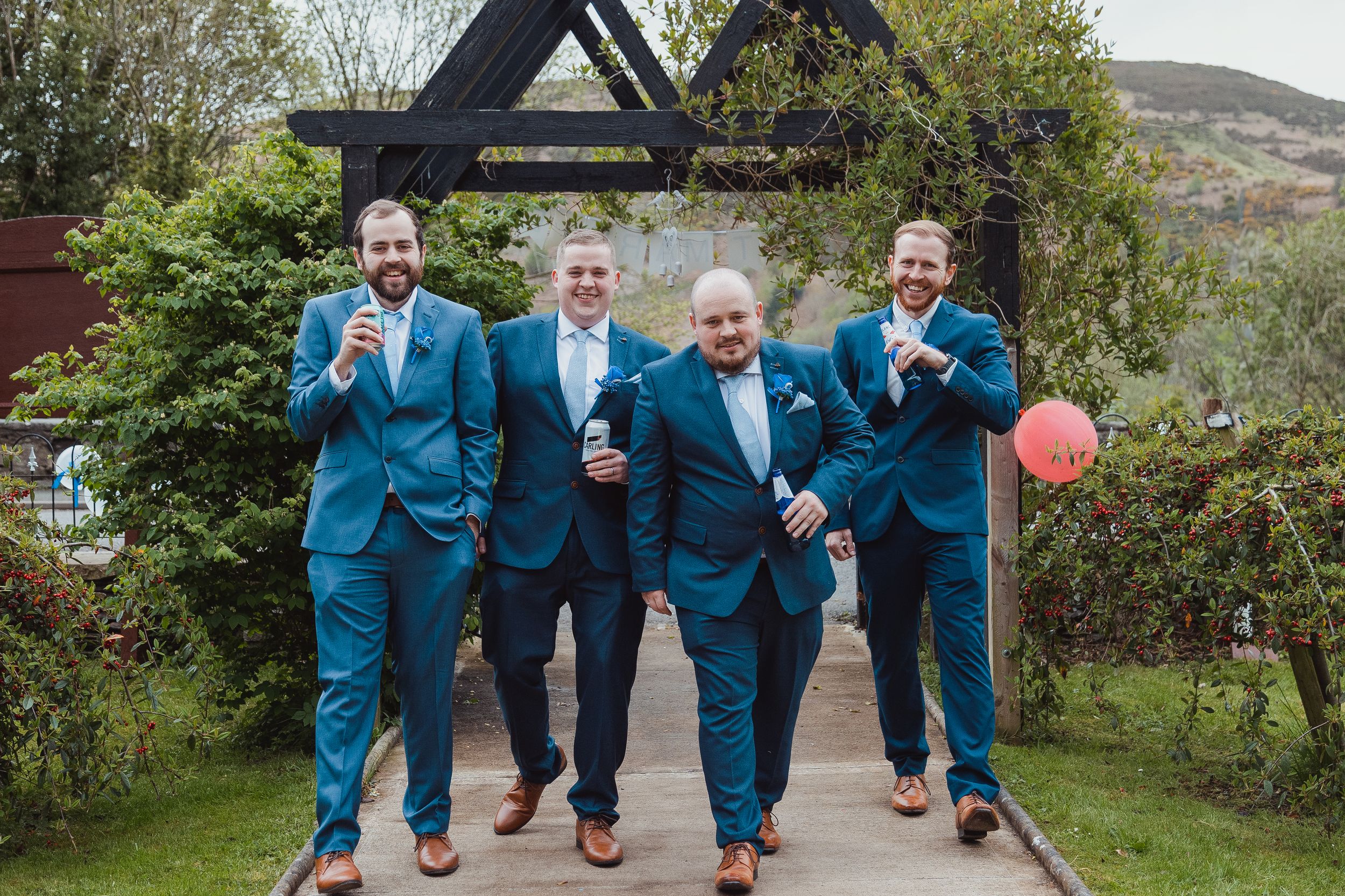 Groomsmen in matching blue suits playfully jumping and posing for a group photo outdoors.