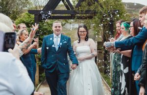 Wedding party celebrating with confetti and laughter in an outdoor garden setting.