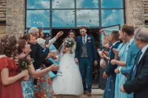 Wedding guests throwing confetti as the newlyweds exit through a historic brick building.