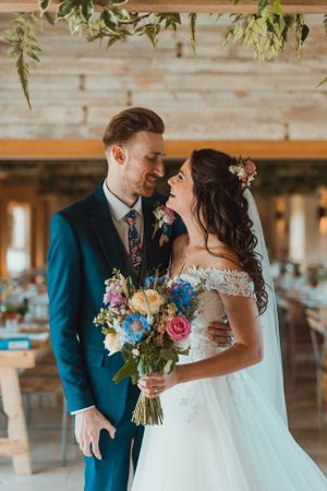 A wedding couple sharing an intimate moment with colorful floral bouquet in an indoor venue.