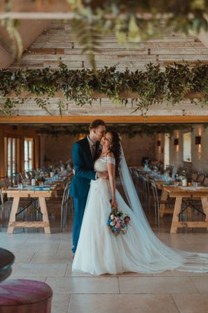 Romantic wedding couple dancing in a rustic barn venue decorated with hanging greenery.