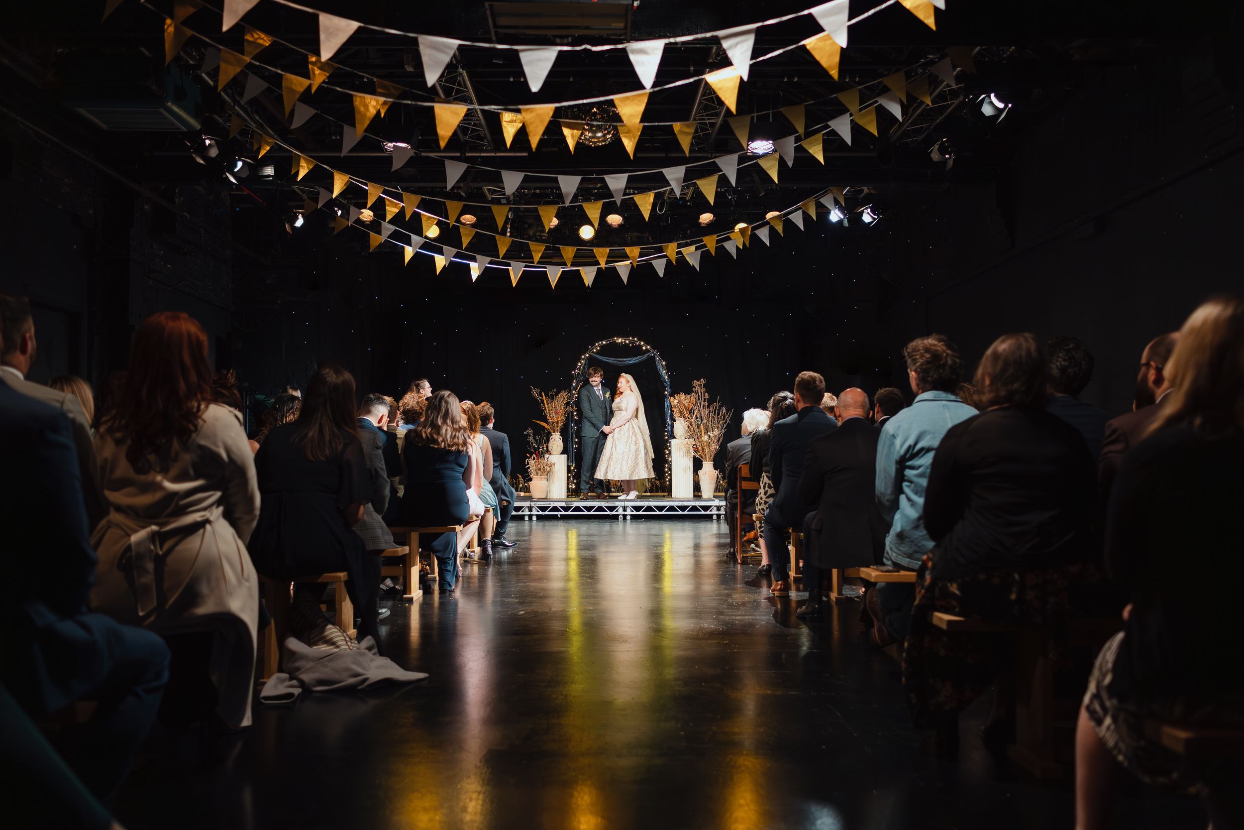 Festive bunting banners hang overhead in a dark event space with people gathered below.
