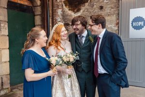 Wedding party members in navy blue and formal attire share candid moments outside a rustic stone building.
