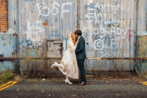 A couple poses against a graffiti-covered brick wall for a romantic urban wedding photoshoot.