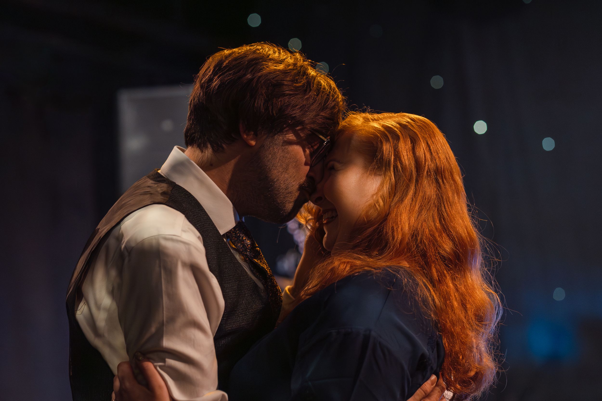 A romantic couple in vintage clothing share an intimate moment with soft lighting and blue bokeh in the background.