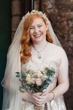 Bride wearing delicate floral crown and champagne lace gown holds elegant bouquet with eucalyptus and cream roses.