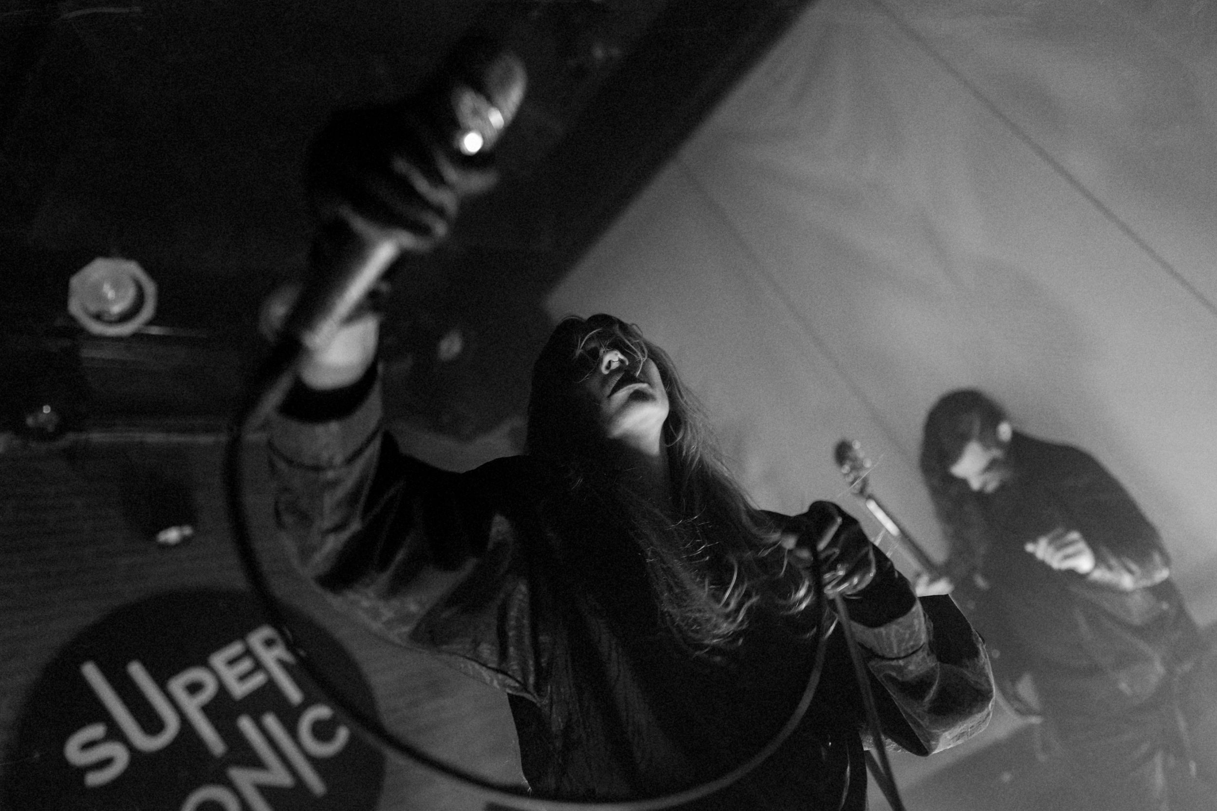 Black and white shot of an energetic live performance at a music venue with a singer holding up a microphone.
