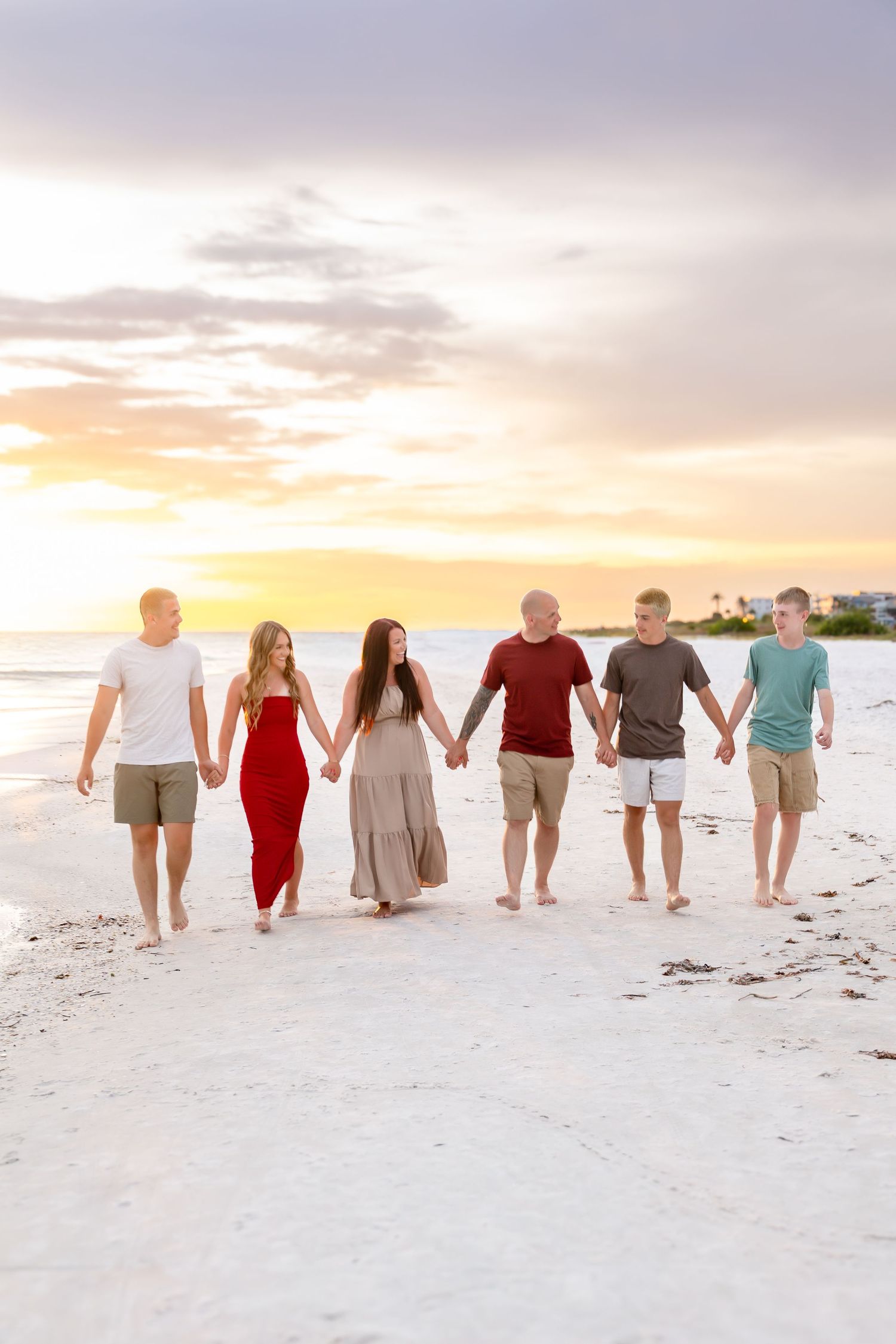 Family of five smiling together barefoot on a sandy beach with ocean waves behind them.