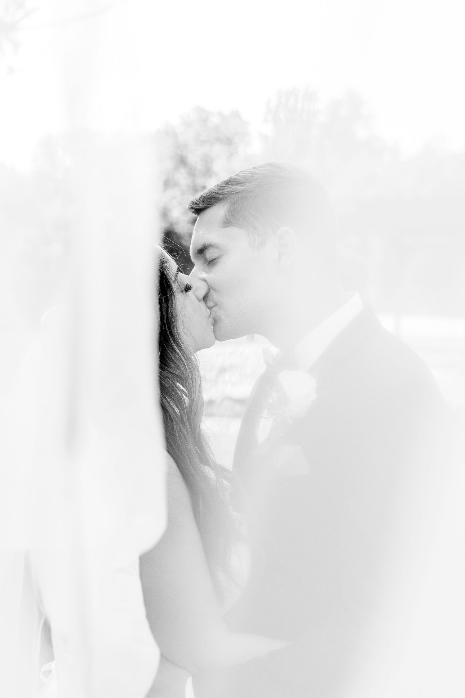 A joyful couple shares a tender moment under a white gazebo, with the bride holding a vibrant pink and white bouquet.