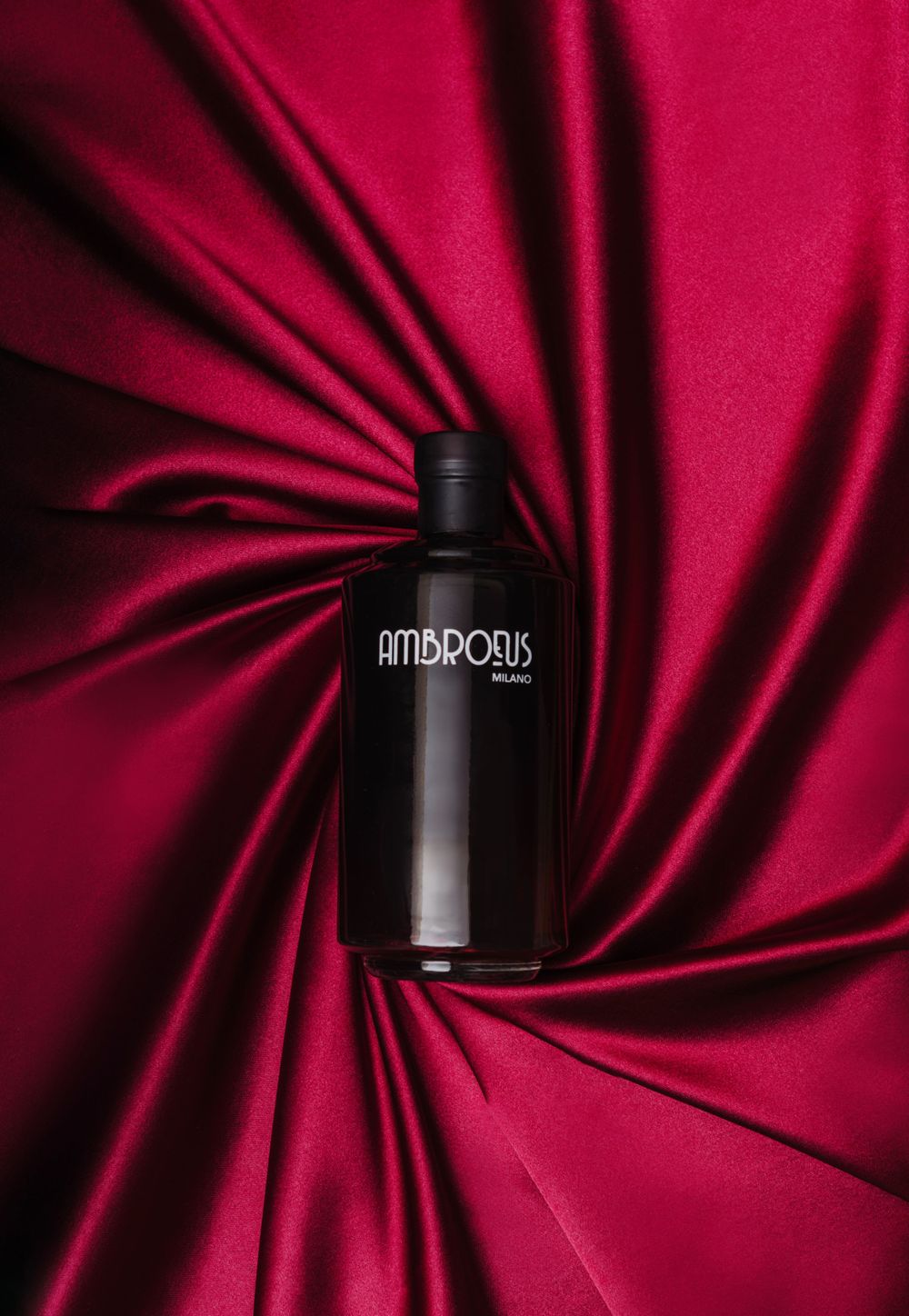 Black Antipodes bottle on swirled red silk fabric with dramatic lighting and shadows.