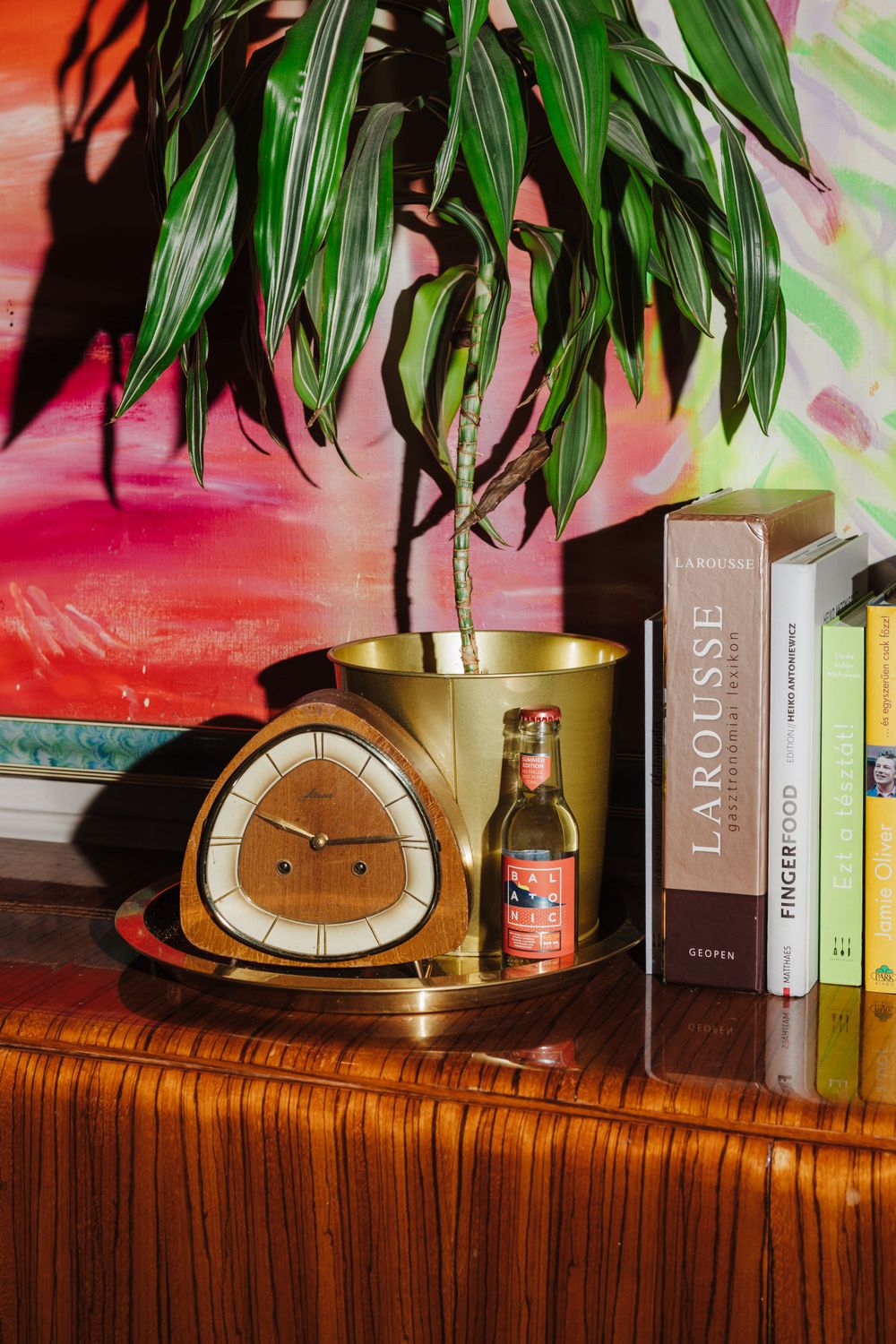 Vintage clock and books displayed with indoor plant against colorful wall art.