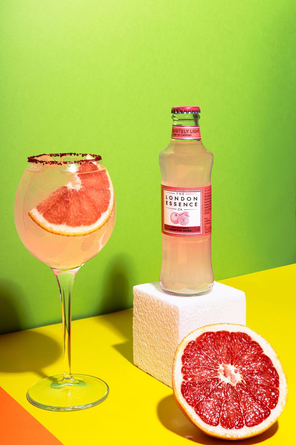 Pink grapefruit cocktail with French Tonic bottle on colorful geometric background.