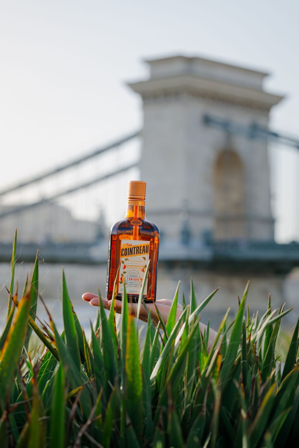 Bottle of Cointreau photographed with Chain Bridge landmark in Budapest background.