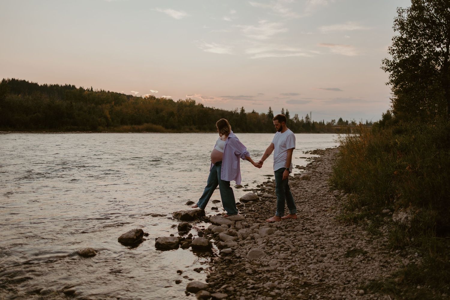 Silhouettes walking along a rocky shoreline at sunset beside a peaceful lake.