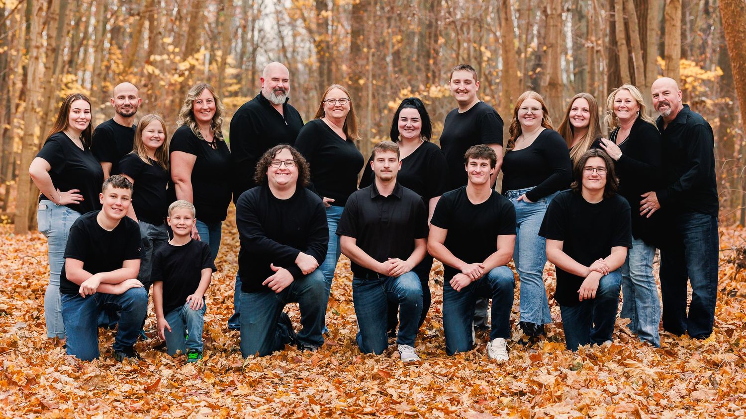 Large family group in black clothing poses together on fallen autumn leaves.