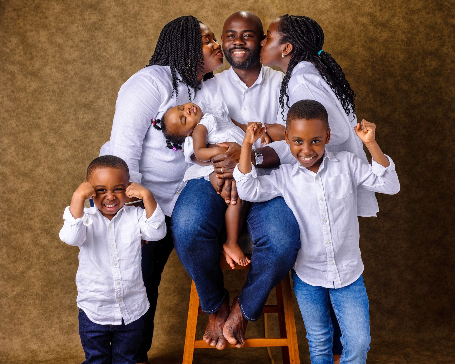 Family portrait of group in white shirts and jeans sitting together on wooden chairs.