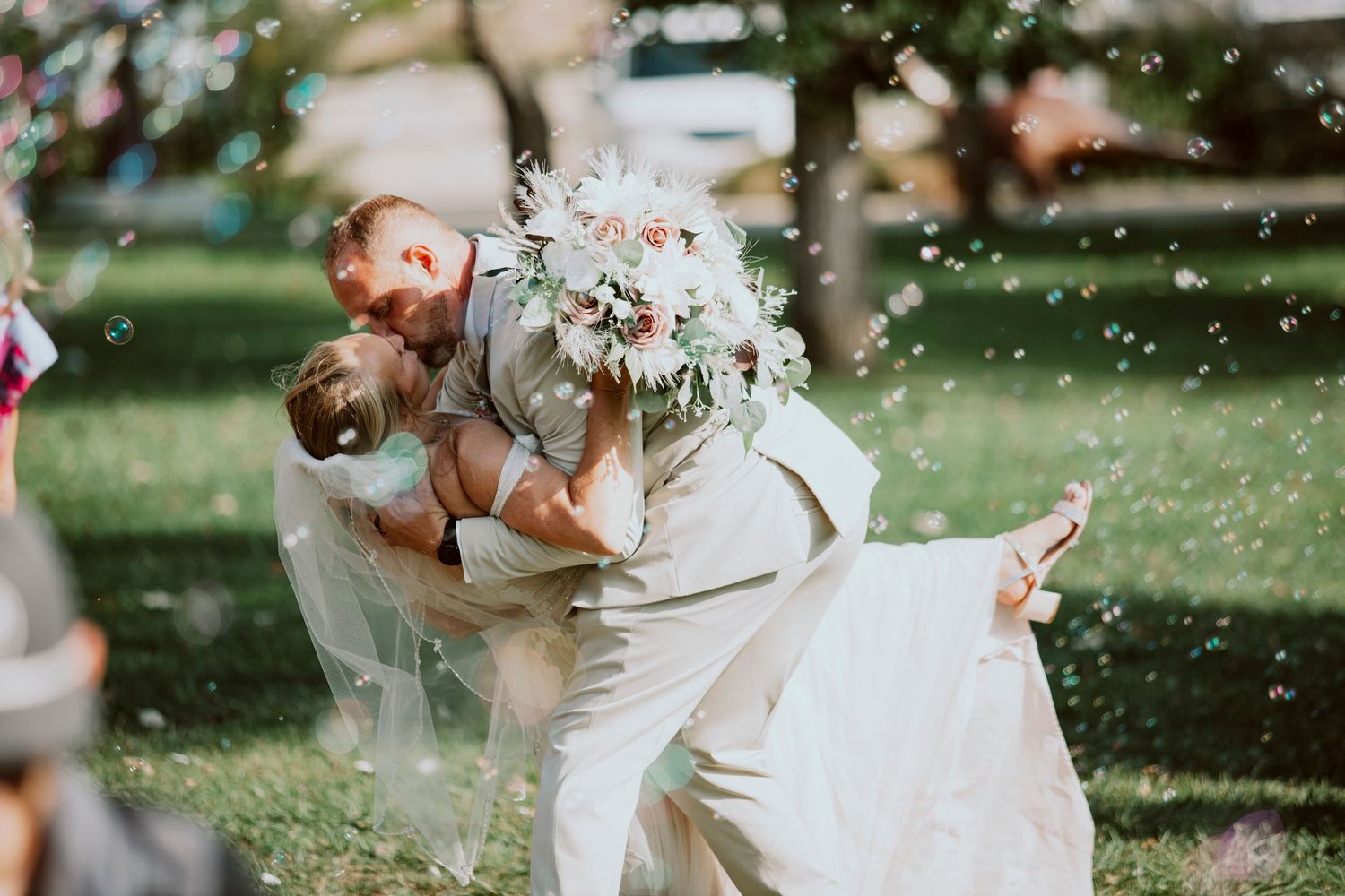A couple in light-colored formal attire share a joyful embrace during their outdoor garden wedding ceremony.