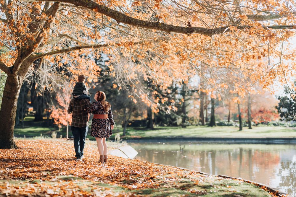 Couple walking hand-in-hand along a serene autumn lake path, surrounded by vibrant orange and yellow foliage.