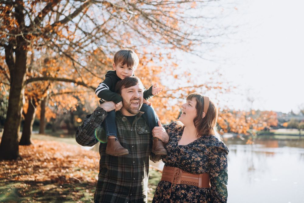 Happy family enjoying a sunny autumn day by a lake with colorful fall trees.