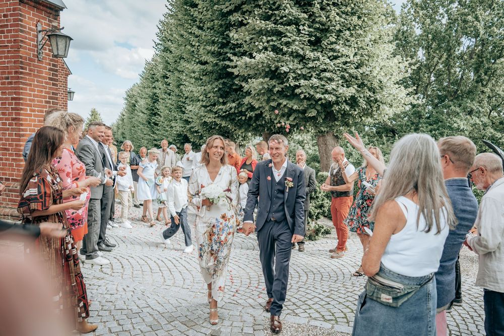 Brudepar går ud af kirken omgivet af glade gæster – romantisk bryllupsøjeblik fotograferet i Frederikssund, Jægerspris og Nordsjælland.