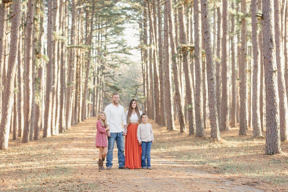 A group poses together on a path lined with tall pine trees in a scenic forest setting.