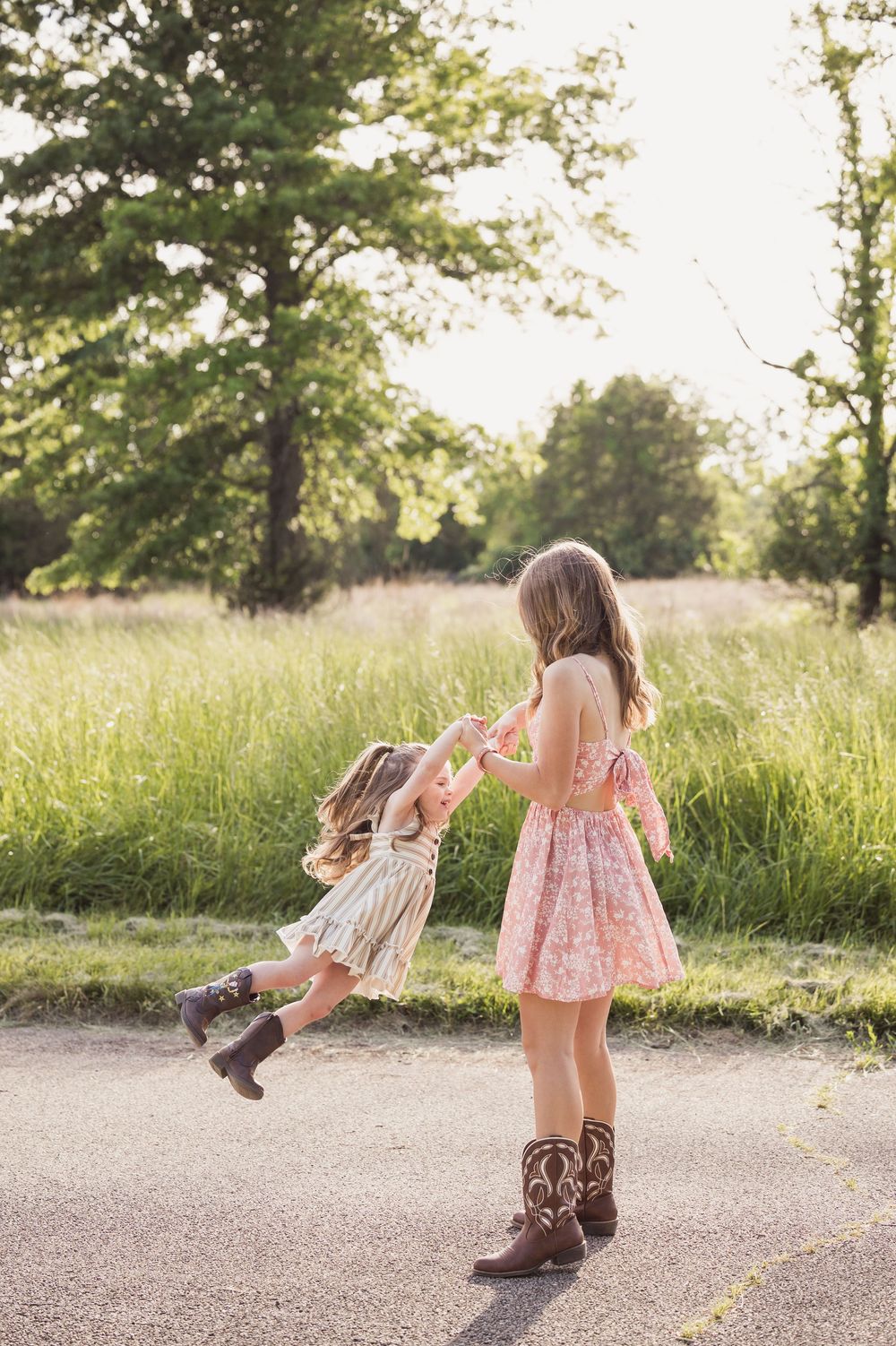 Two children playing together on a path surrounded by tall grass and trees in golden afternoon sunlight.