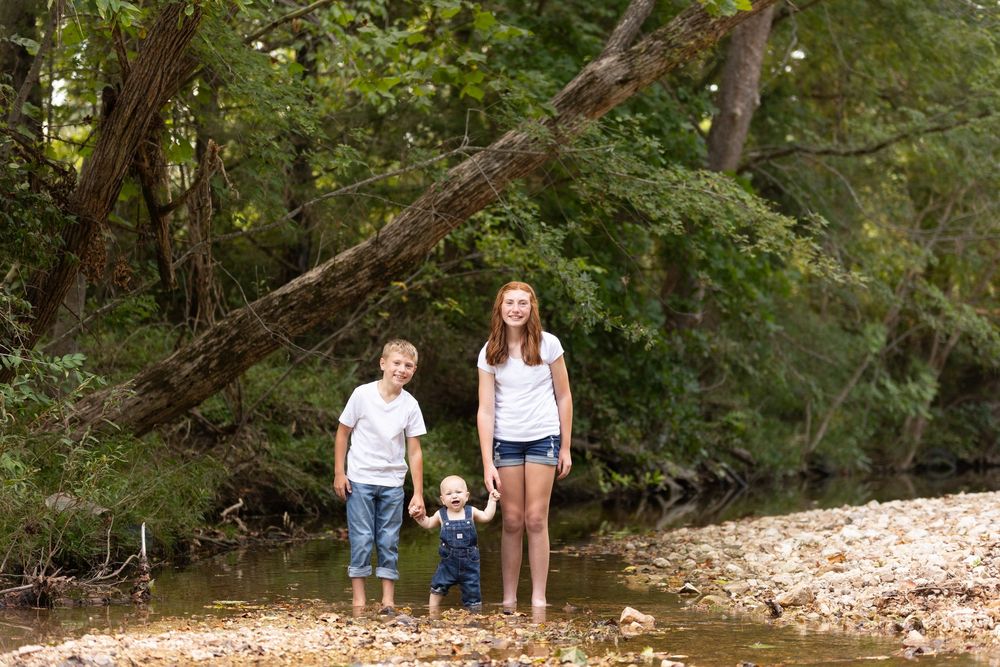 A group explores a rocky creek bed surrounded by lush green forest on a summer day.