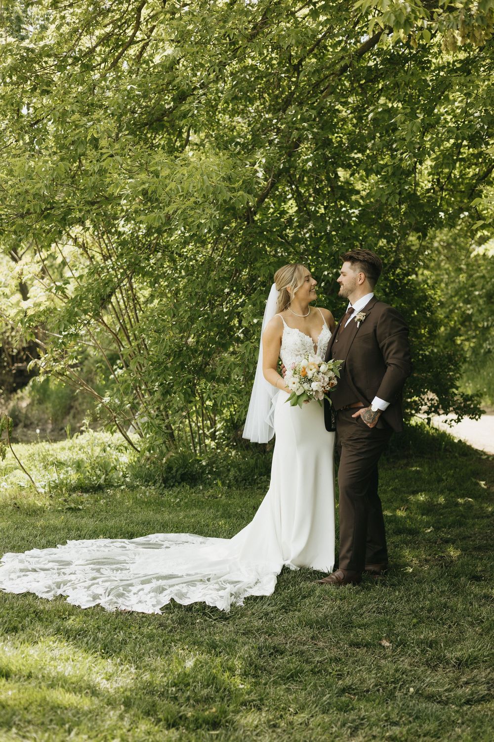 A bride and groom share an intimate moment in a lush garden setting with a flowing white wedding dress train.